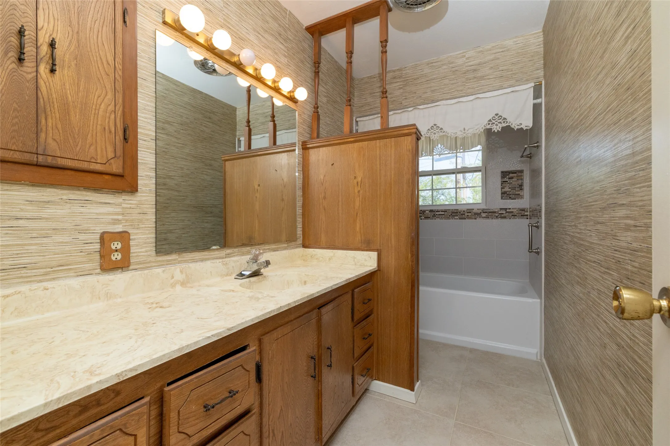 Built-in wooden cabinetry with a light-toned countertop, a full vanity mirror, and a white bathtub with subway tile surround