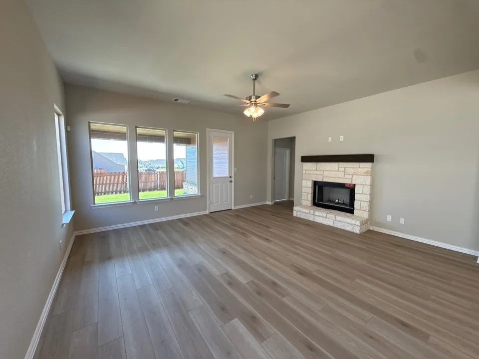 Spacious living area featuring wood-finish flooring, a stone fireplace with a wood mantel, and a ceiling fan