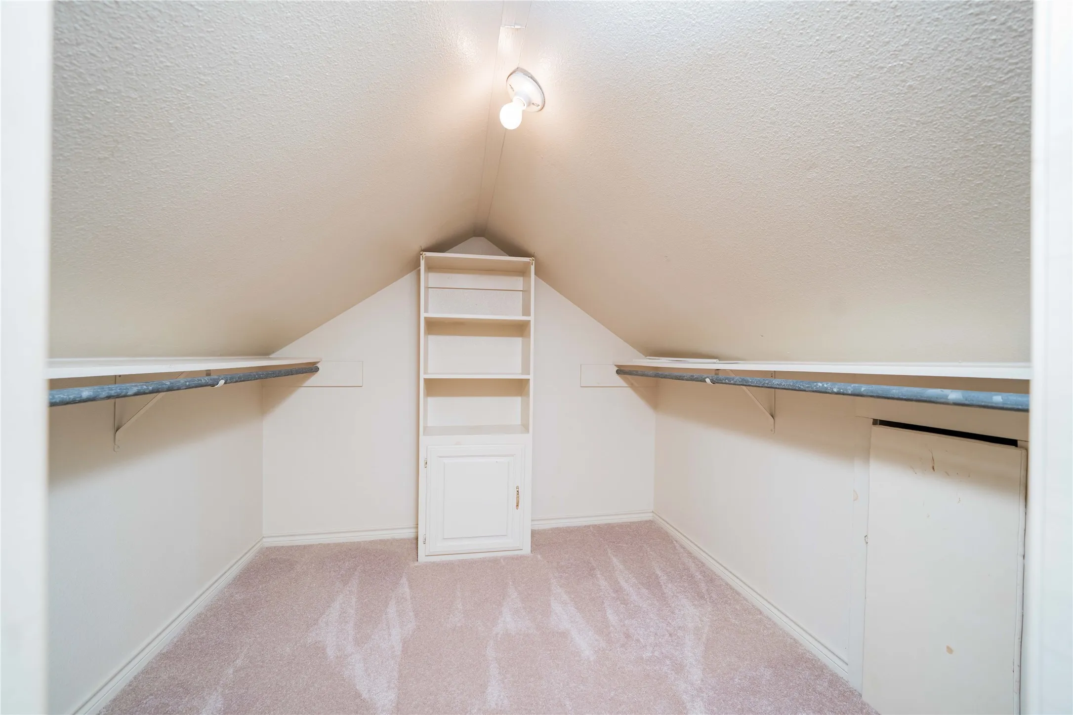 Carpeted attic space featuring sloped ceilings, built-in shelving with lower cabinetry, and dual clothing rods