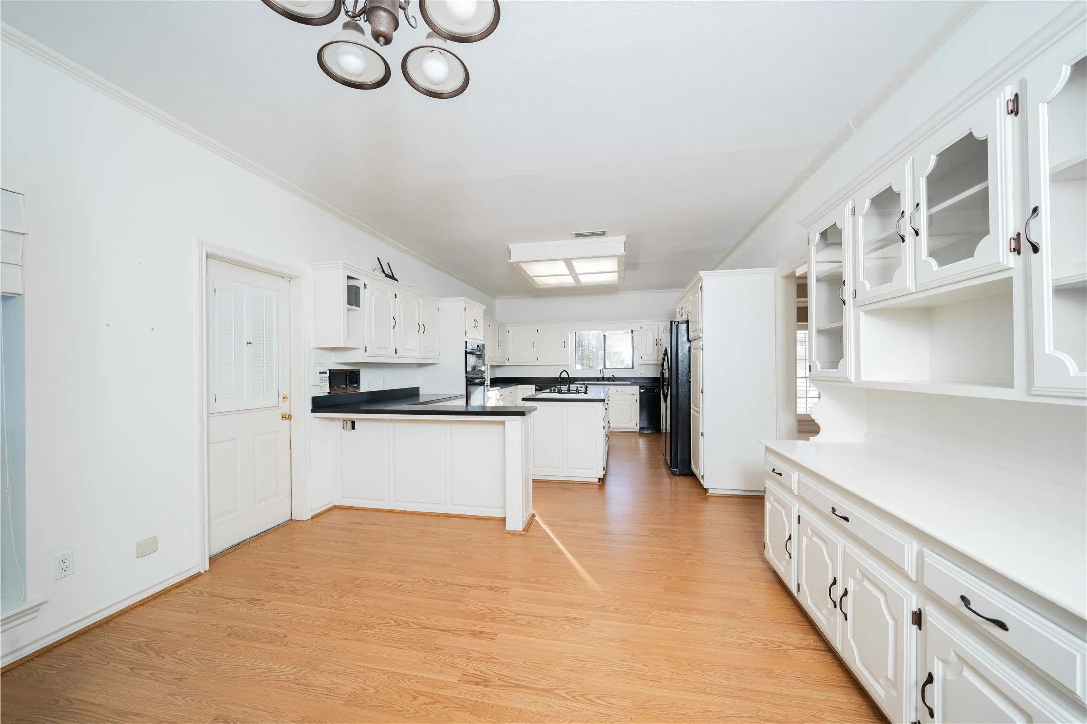 Spacious kitchen with wood-finish flooring, abundant white cabinetry, integrated island with seating, dark countertops, and built-in display shelving