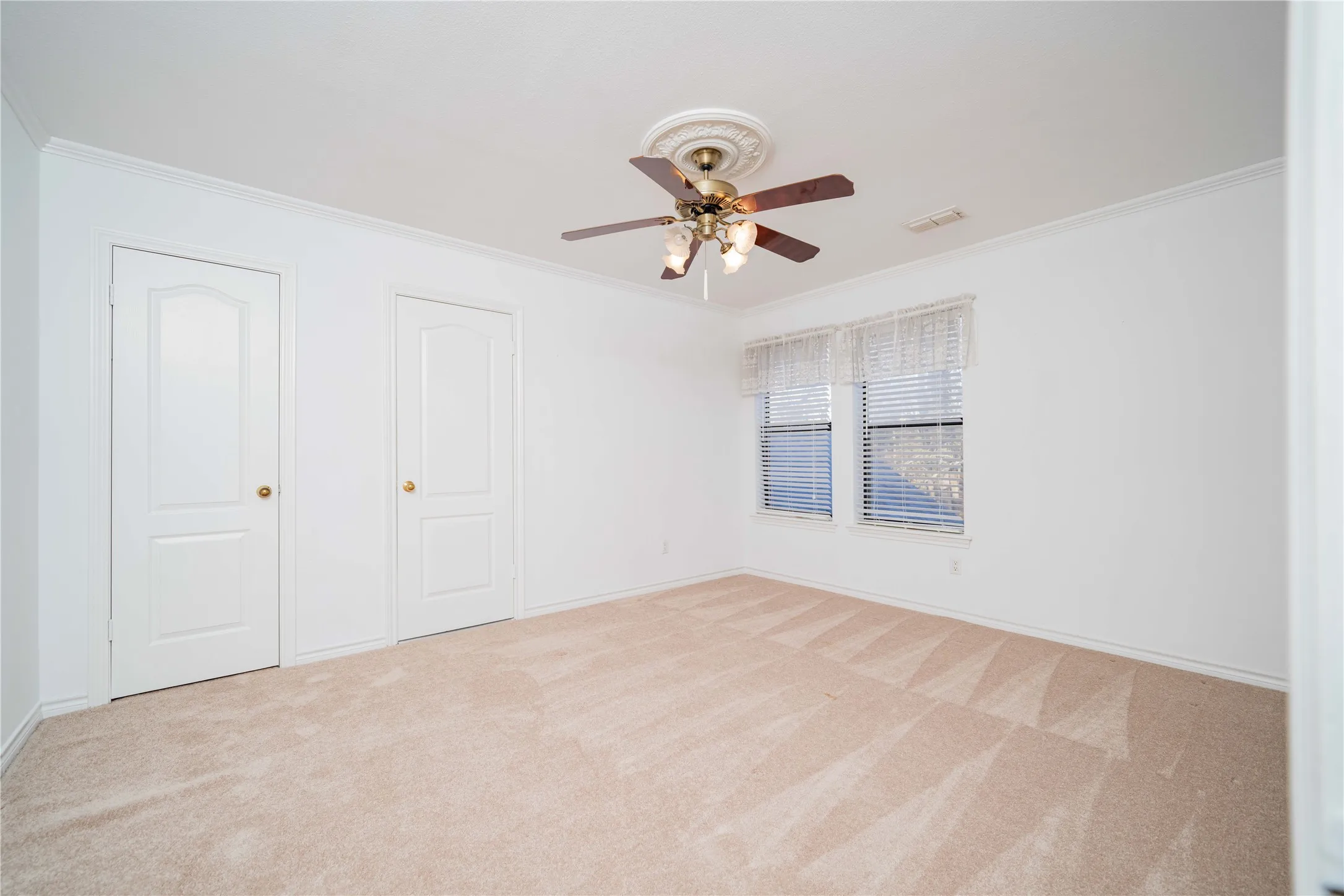 Light-filled room featuring neutral-toned carpet, crown molding, and two panel doors with brass hardware