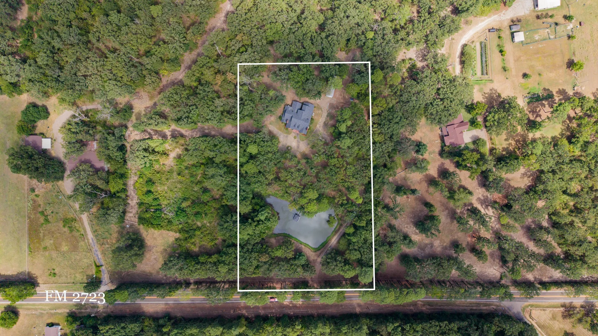 Aerial property showcasing a main residence, an additional structure, and a private pond amidst dense tree coverage