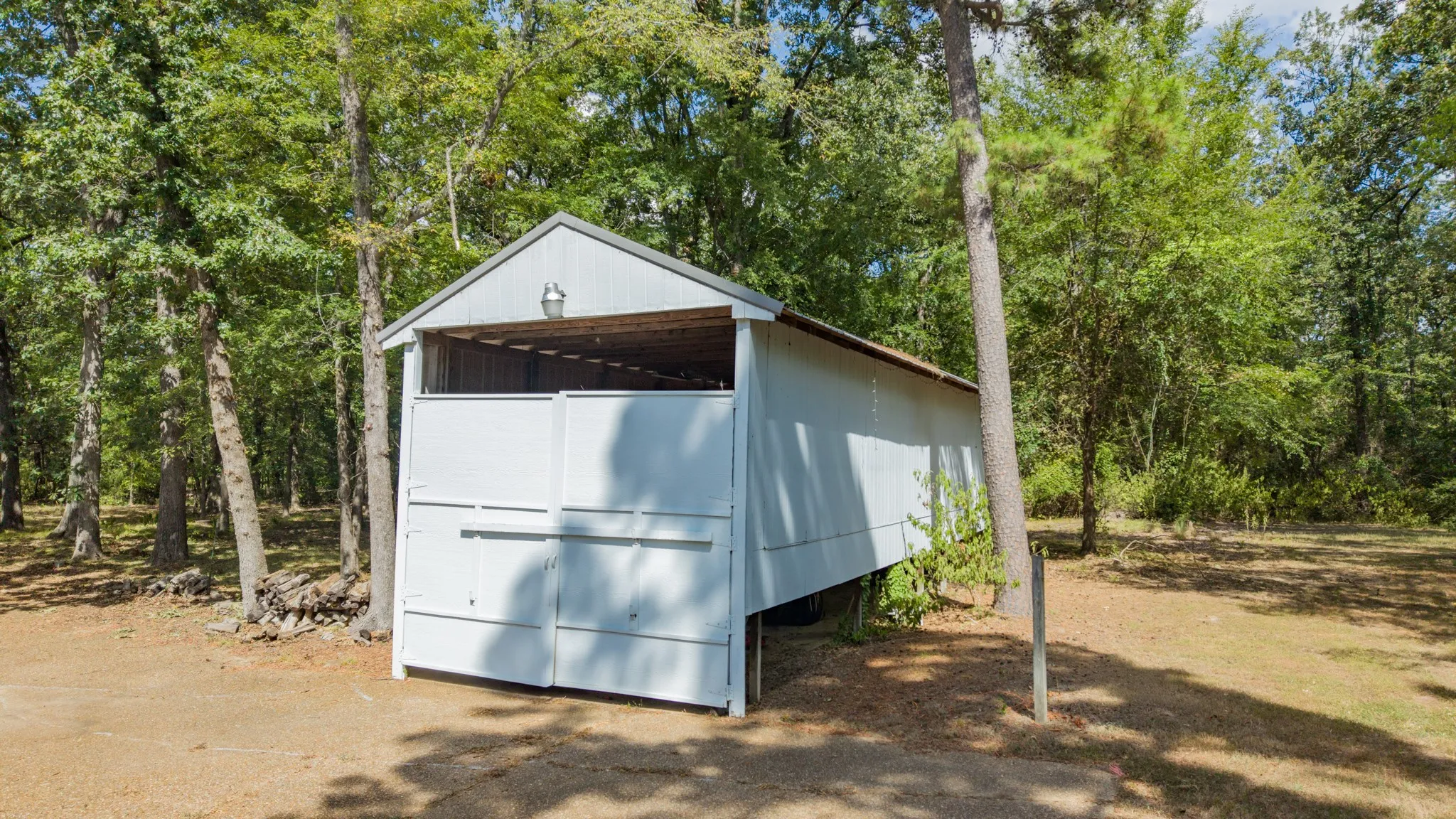 Open-air barn structure with a metal roof and white siding, featuring a gravel ground surface