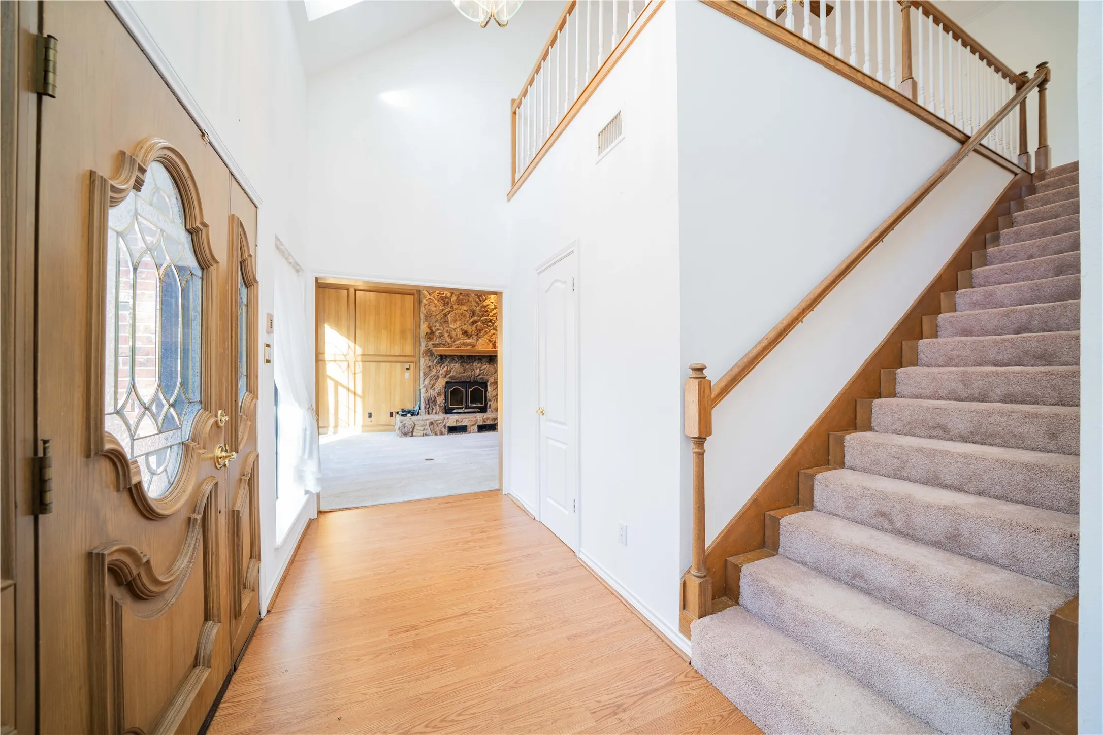 Foyer featuring a grand carved wood entry door with leaded glass details, wood-finish flooring, a two-story ceiling, and a carpeted staircase with wood railings