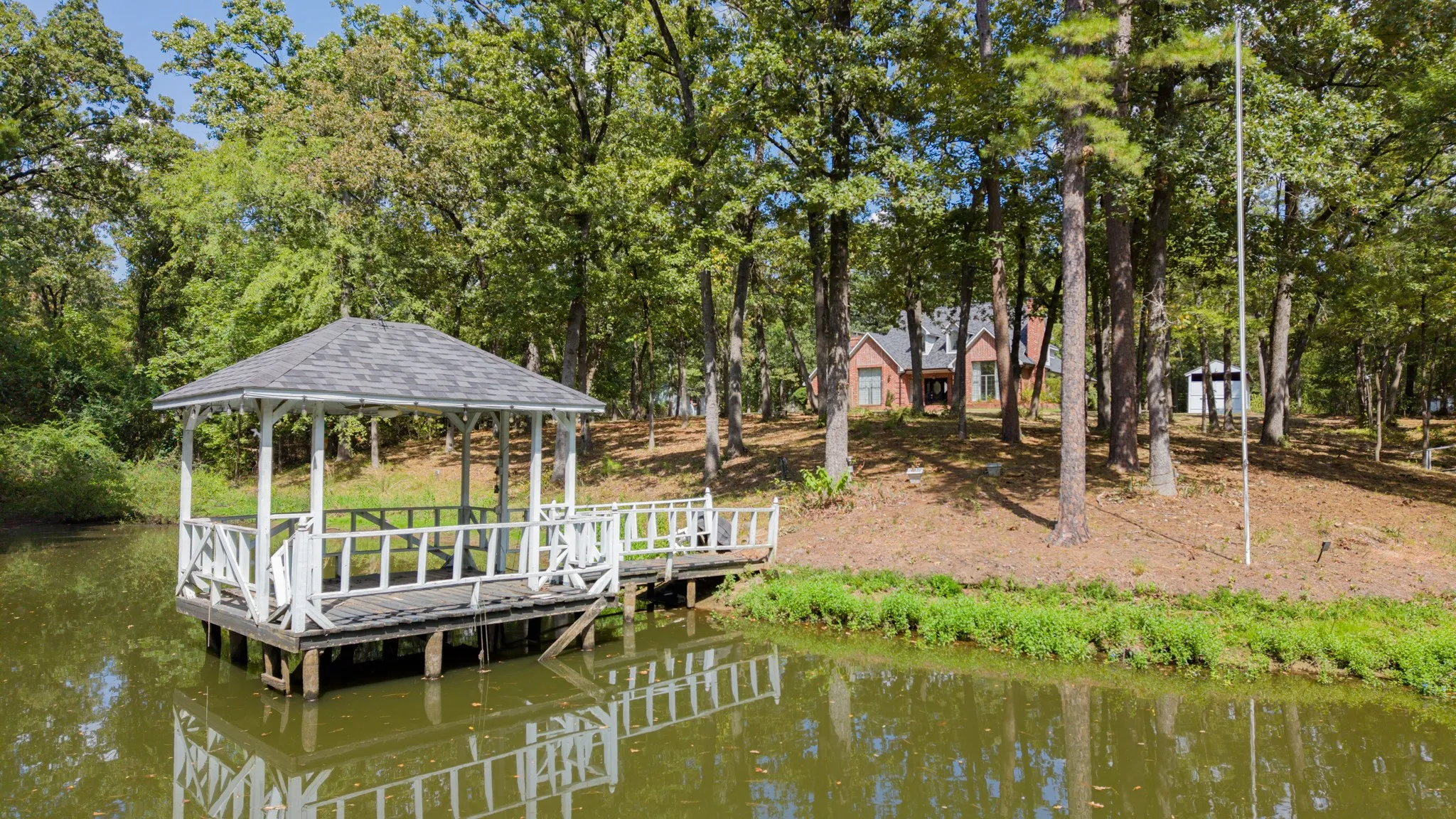 Waterfront gazebo with a shingled roof, an expansive wooded lot, and a brick exterior residence
