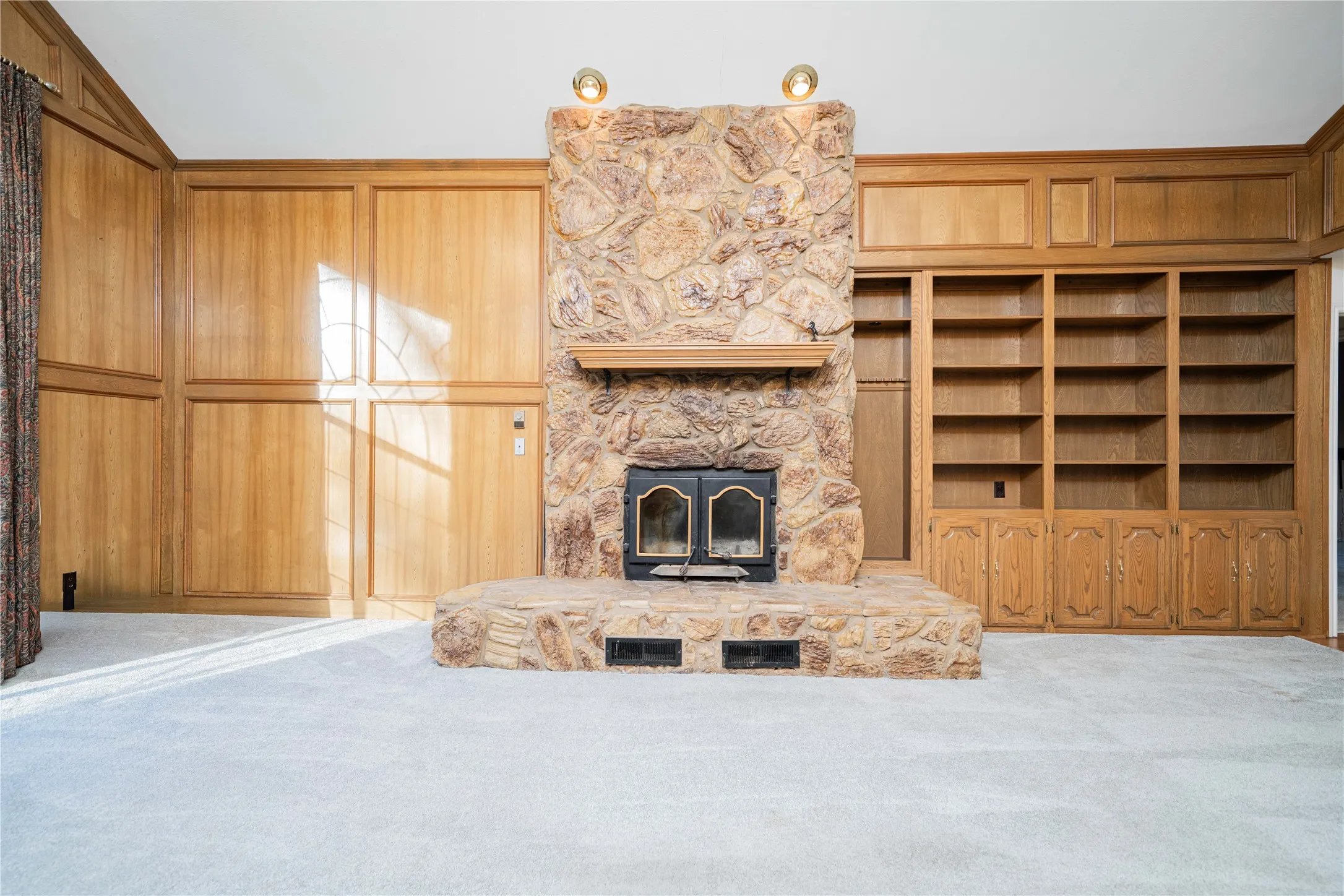 Stone-clad fireplace with a wood mantel and hearth, flanked by extensive built-in wooden cabinetry and shelving