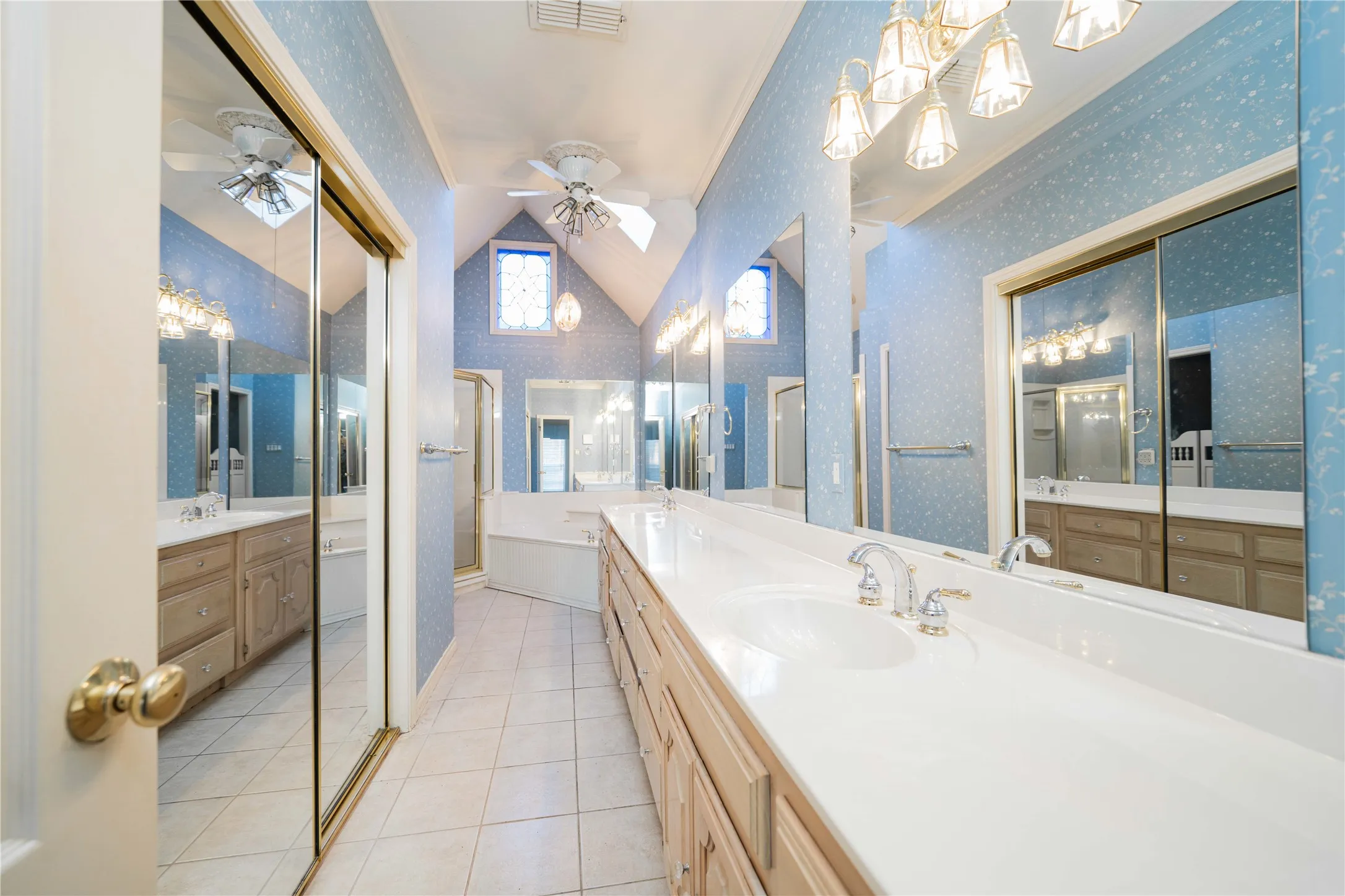 Bathroom featuring a dual vanity with integrated sinks and chrome fixtures, extensive mirrored walls, and light-toned tile flooring