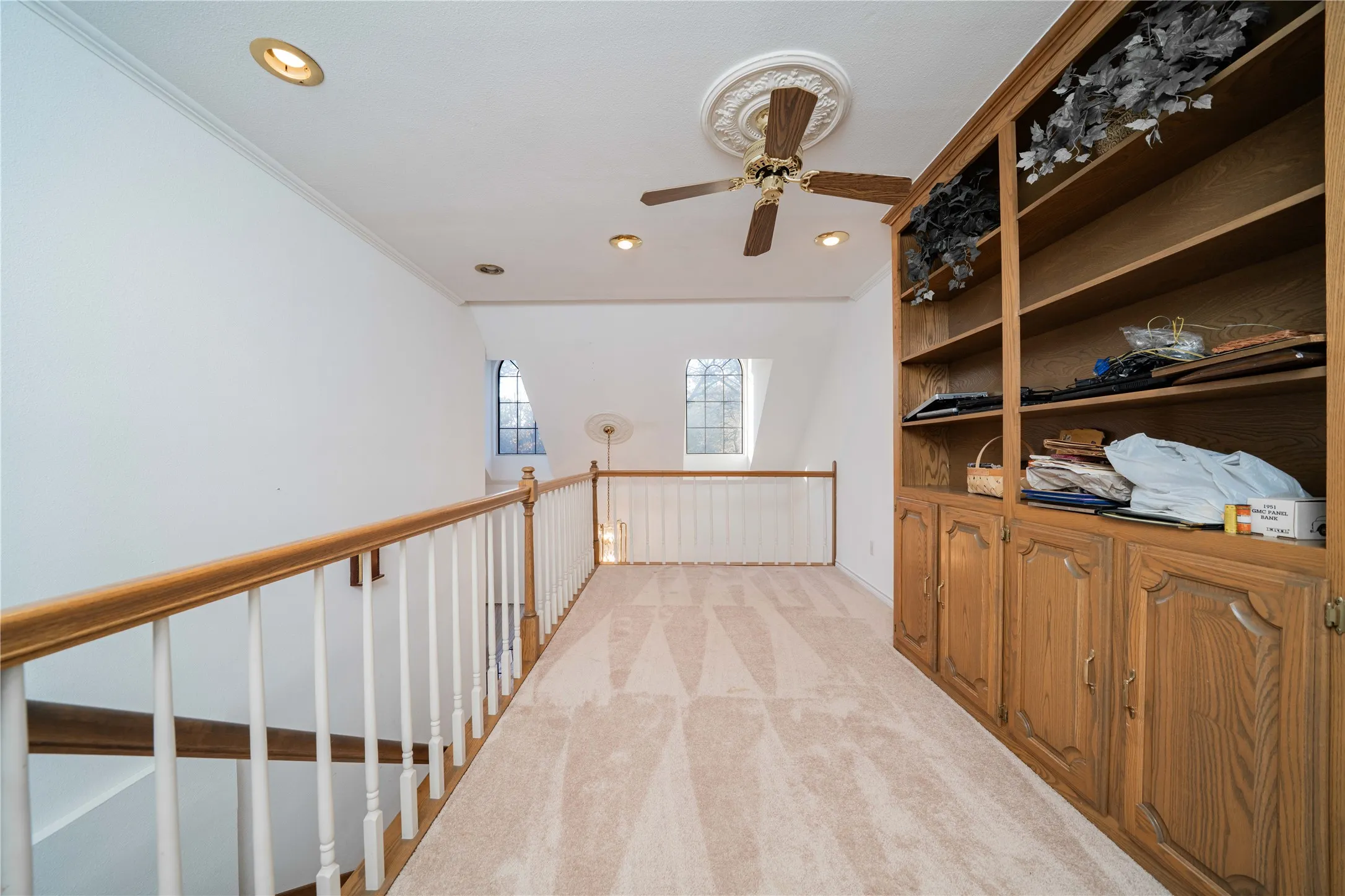 Carpeted loft space featuring a built-in wood-finish shelving unit, recessed lighting, and a ceiling fan with decorative medallion