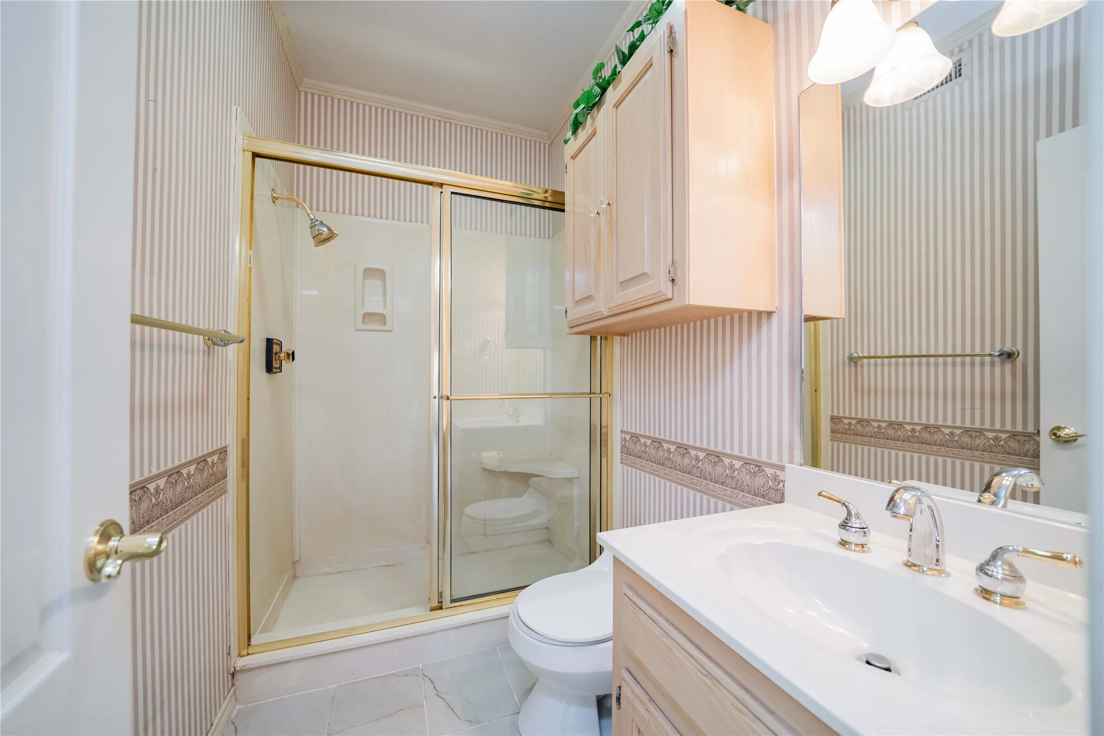 Full bathroom featuring a shower with a gold-toned frame, a white vanity with a built-in sink, and a wall-mounted light fixture above the mirror