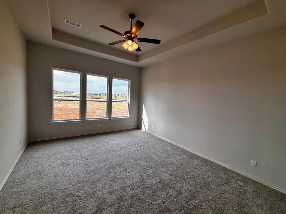 Tray ceiling with a ceiling fan, three pane windows, and neutral carpeting