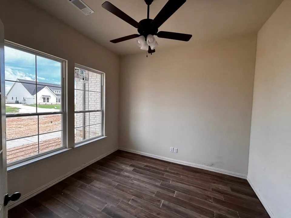 Wood-finish plank flooring, neutral wall tones, two large windows, and a ceiling fan with integrated lighting
