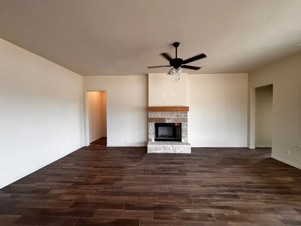 Spacious living area featuring wood-finish flooring, stone-clad fireplace with wood mantel, and an overhead ceiling fan