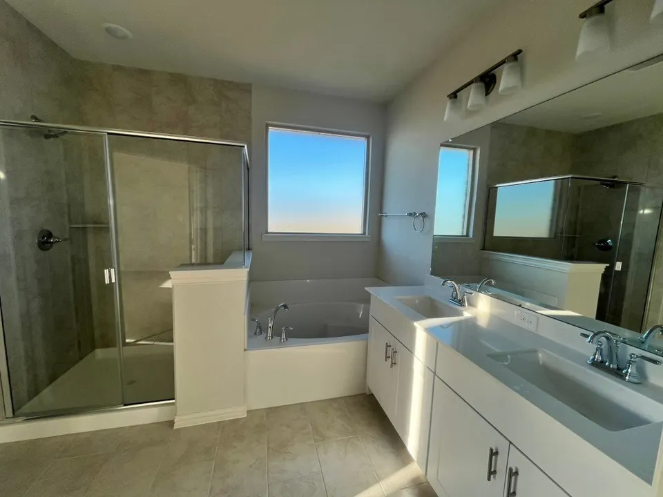 Dual vanity with white cabinetry and integrated sinks, a built-in bathtub, a glass-enclosed shower, and tile flooring