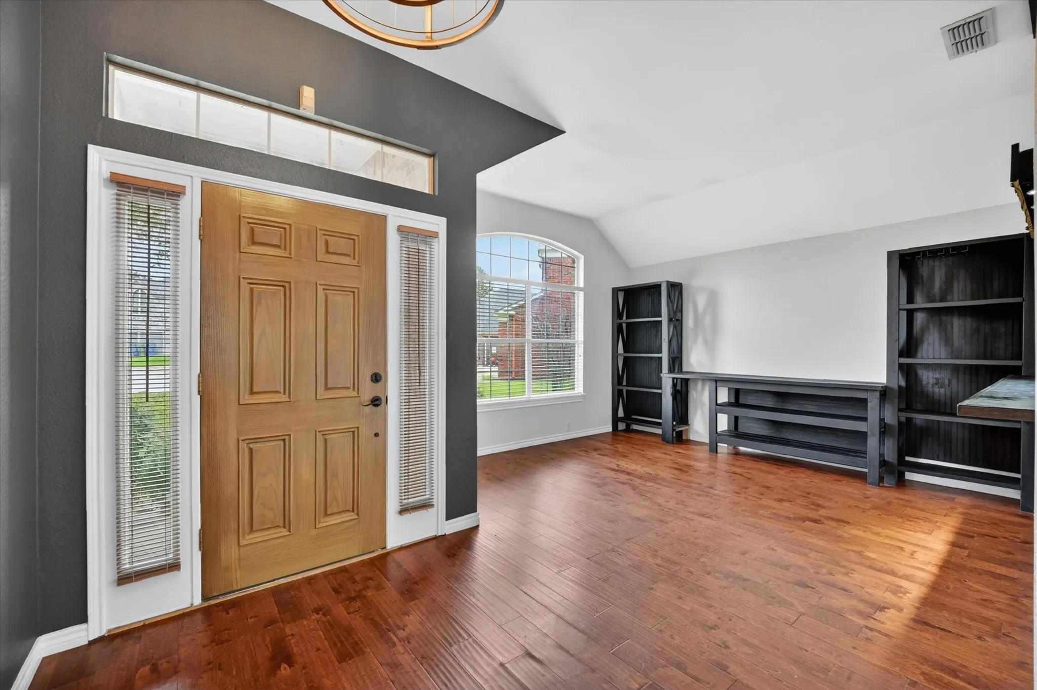 Hardwood-finish flooring, wood entry door with sidelights, transom window, arched window, and vaulted ceiling