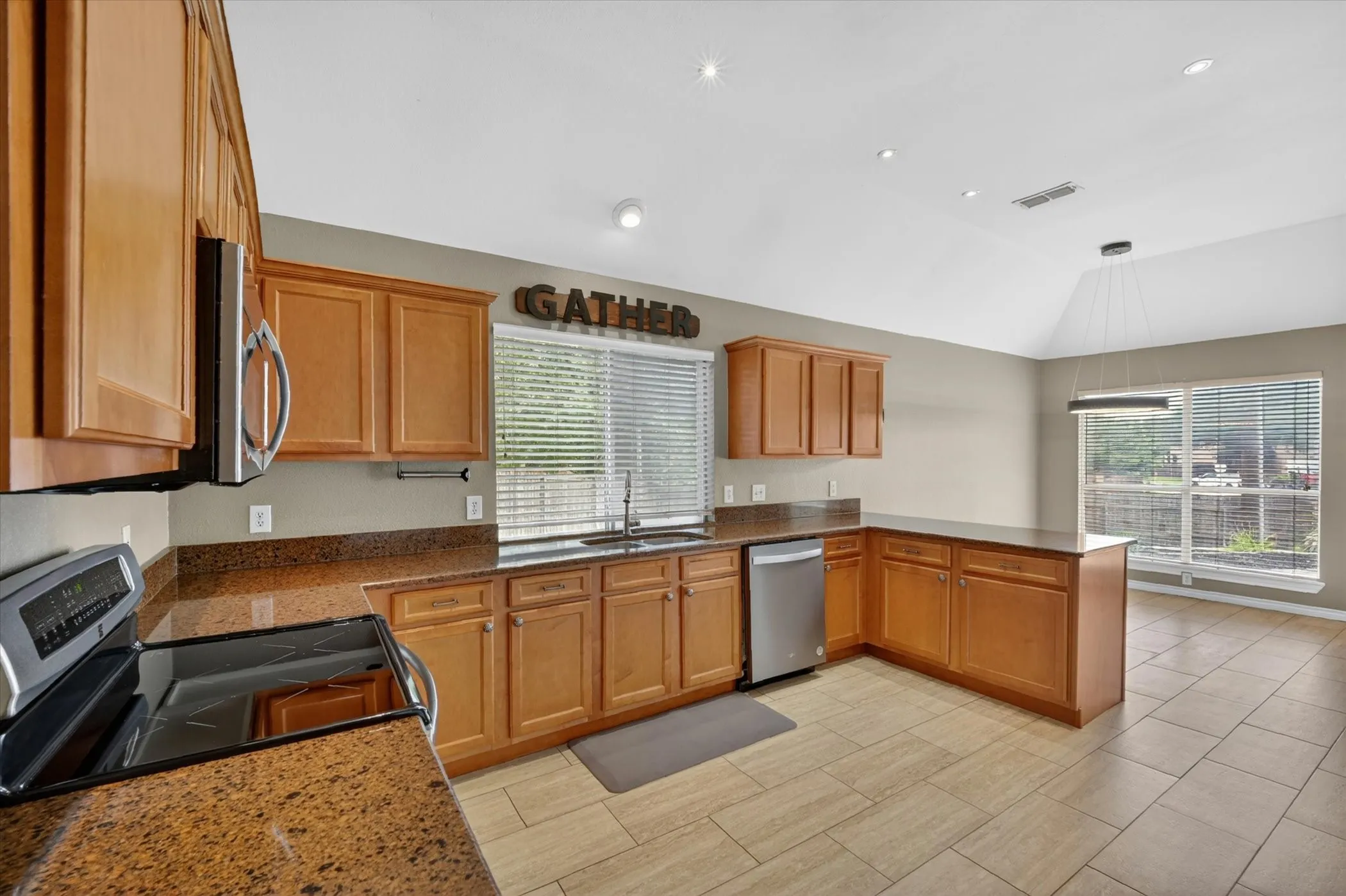 Kitchen featuring wood cabinetry, stainless steel appliances, granite countertops, tile flooring, and a vaulted ceiling