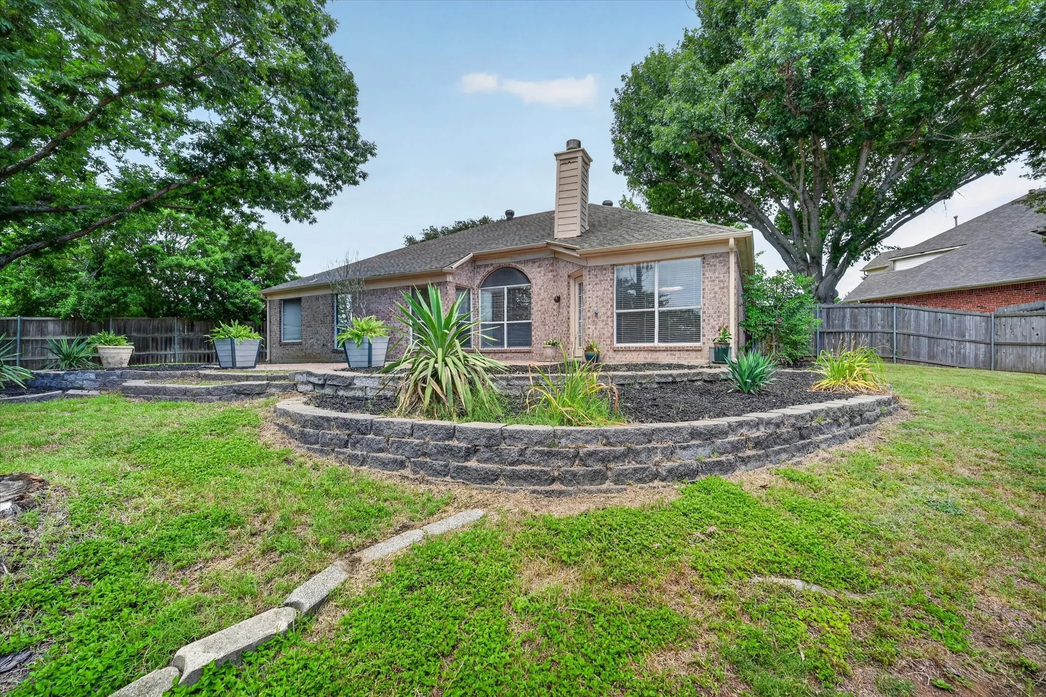 Charming brick residence with mature landscaping and curved stone retaining walls framing the expansive lawn