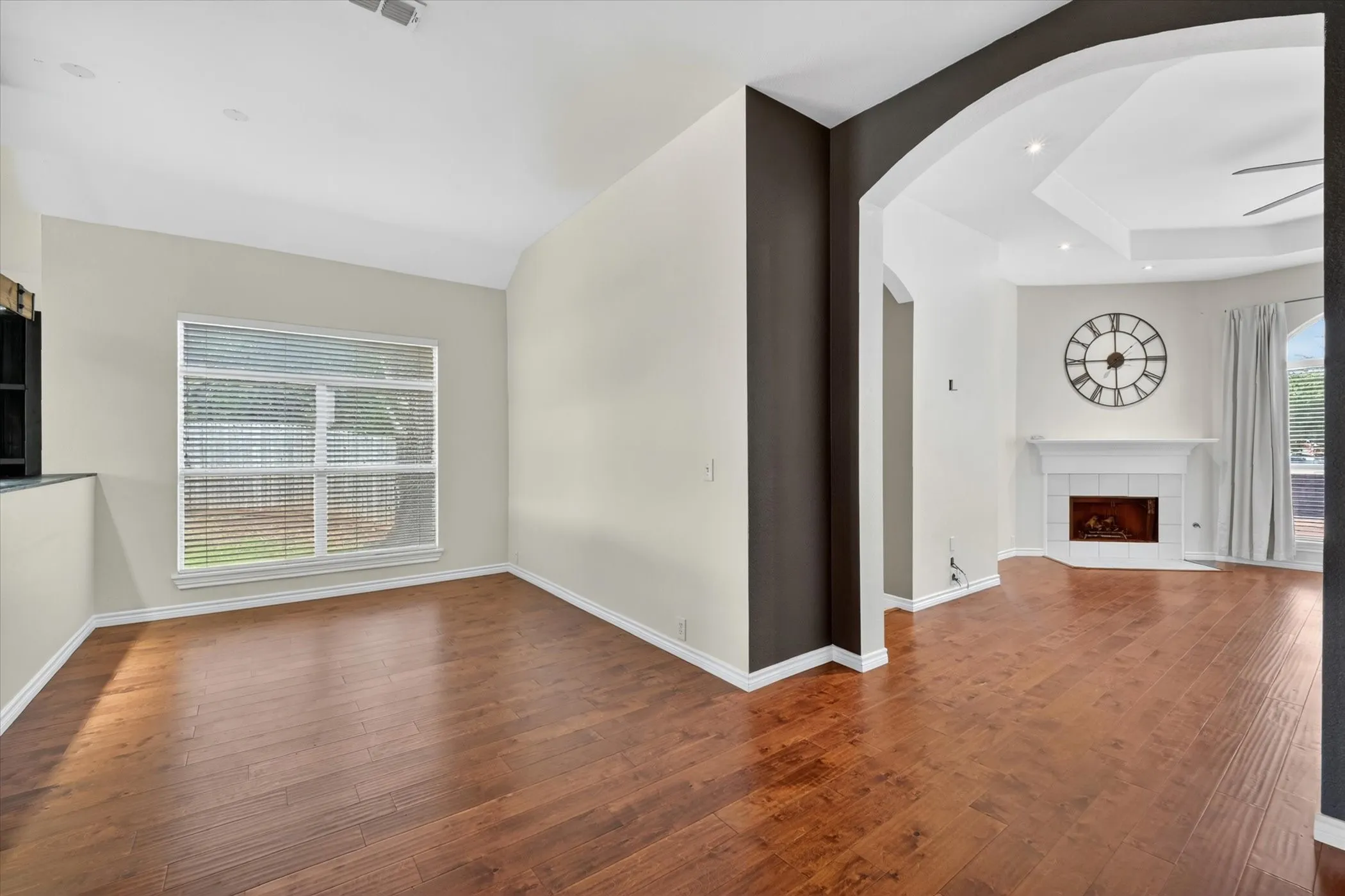 Spacious open-concept living area featuring rich wood-finish flooring throughout, soaring ceilings with recessed lighting, and a striking dark architectural column dividing the space