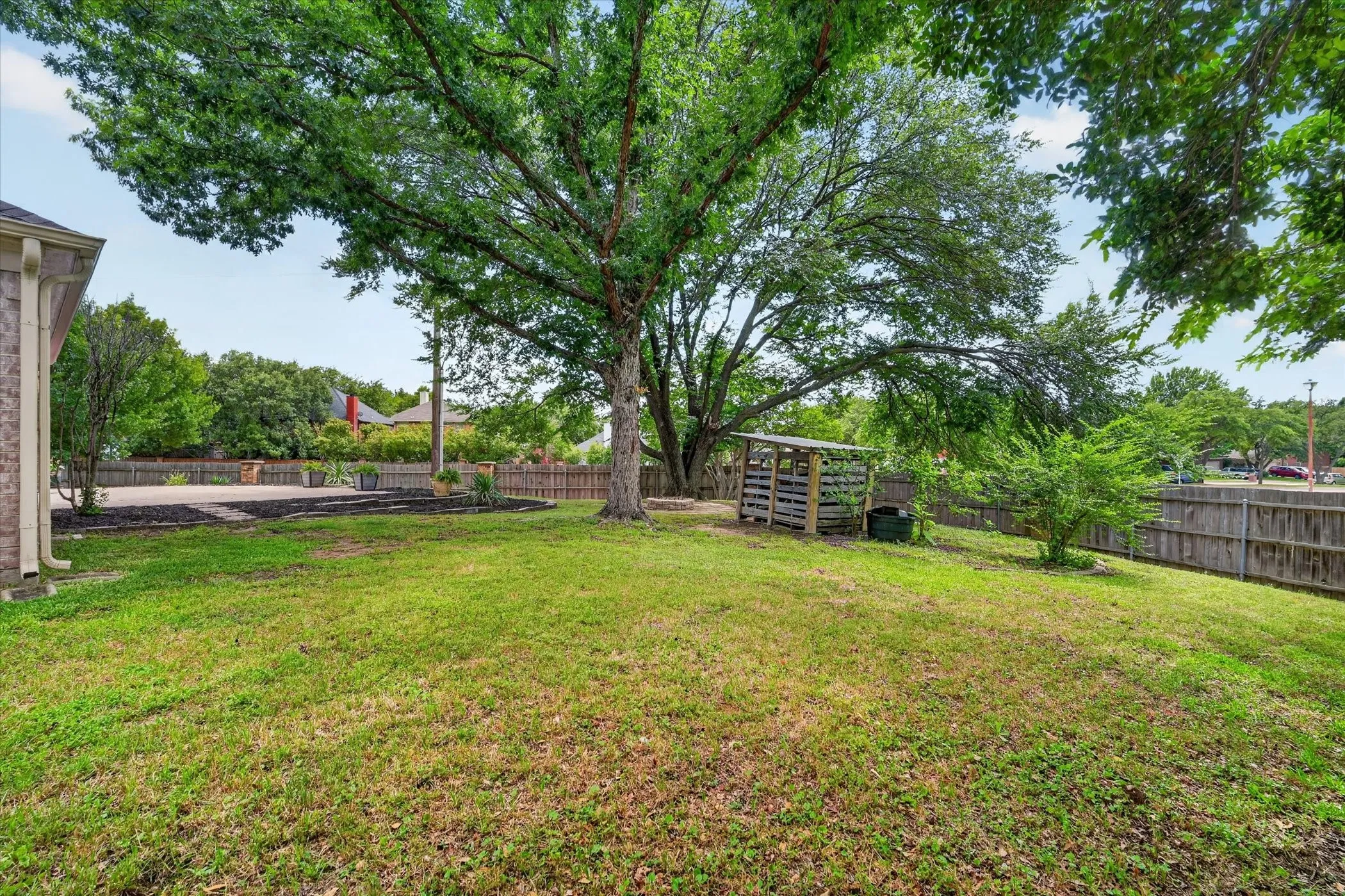 Expansive lawn area with mature trees, wood fencing, and a built-in outdoor structure