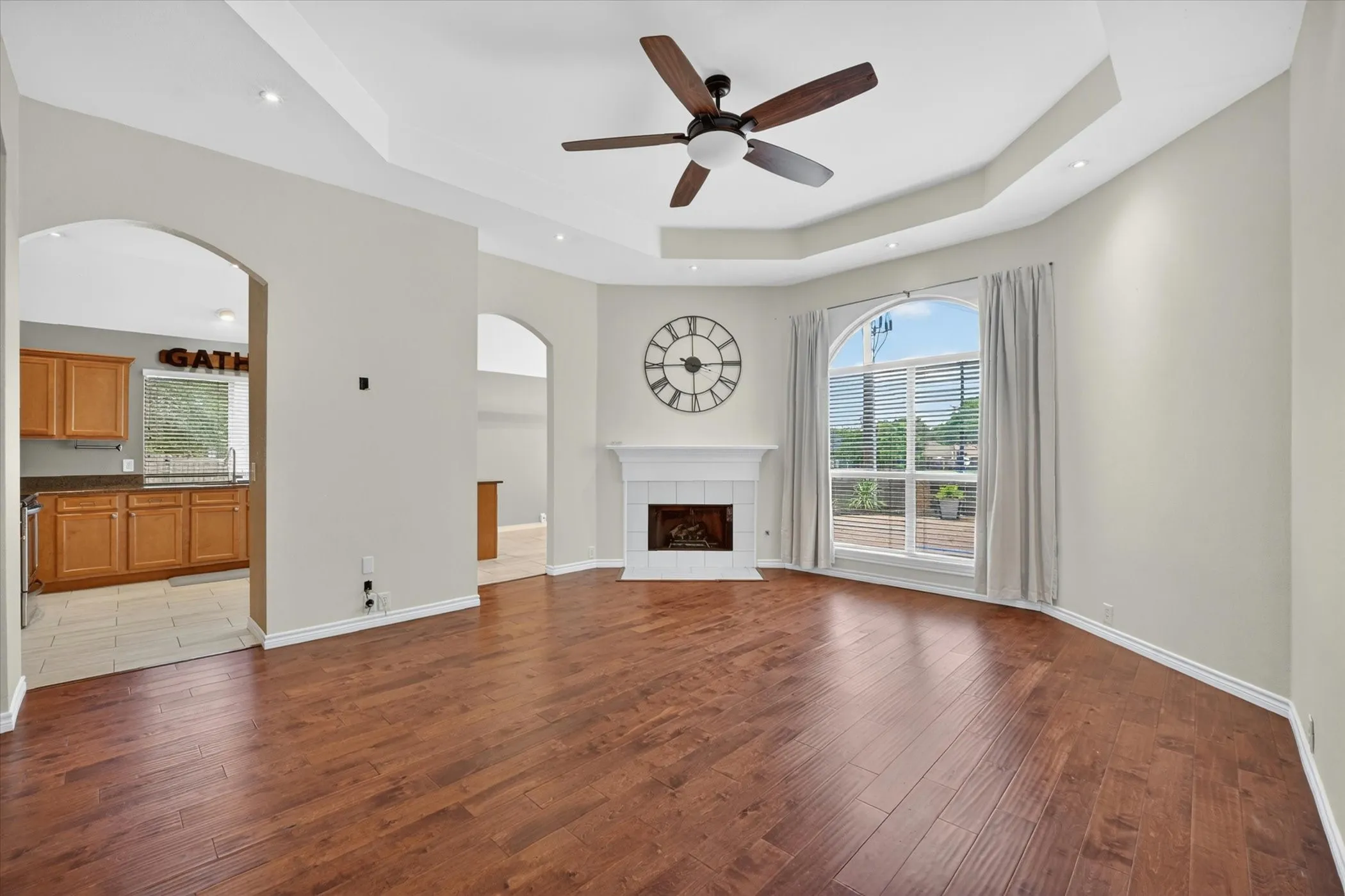 Spacious great room showcasing gleaming wood-finish flooring, a coffered ceiling with ceiling fan, and abundant natural light from multiple windows