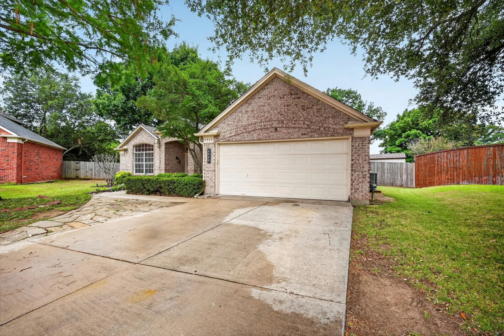 Brick exterior, attached garage, stone pathway, mature landscaping, and a fenced yard