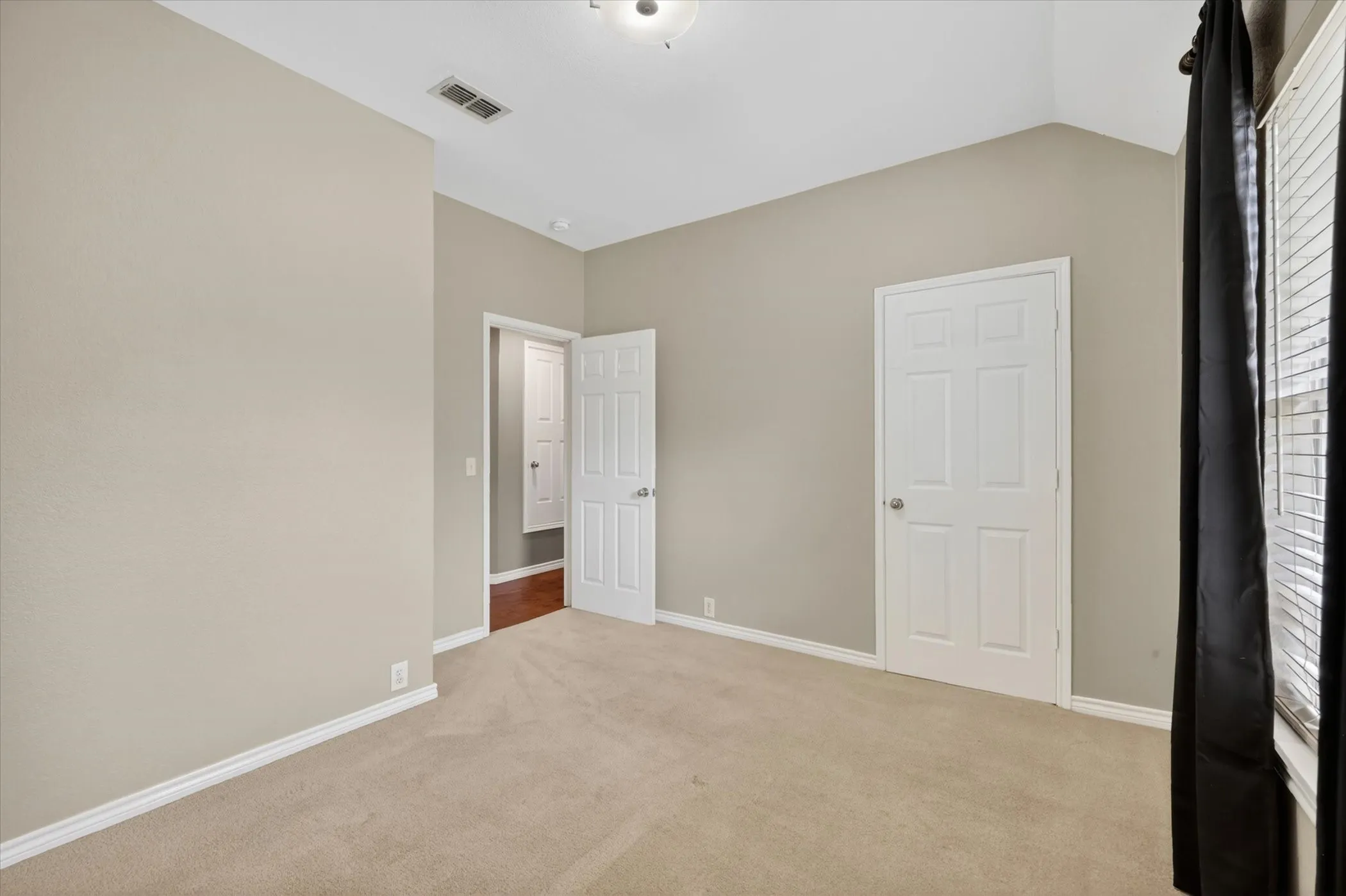 Neutral-toned walls, vaulted ceiling, and plush carpet flooring