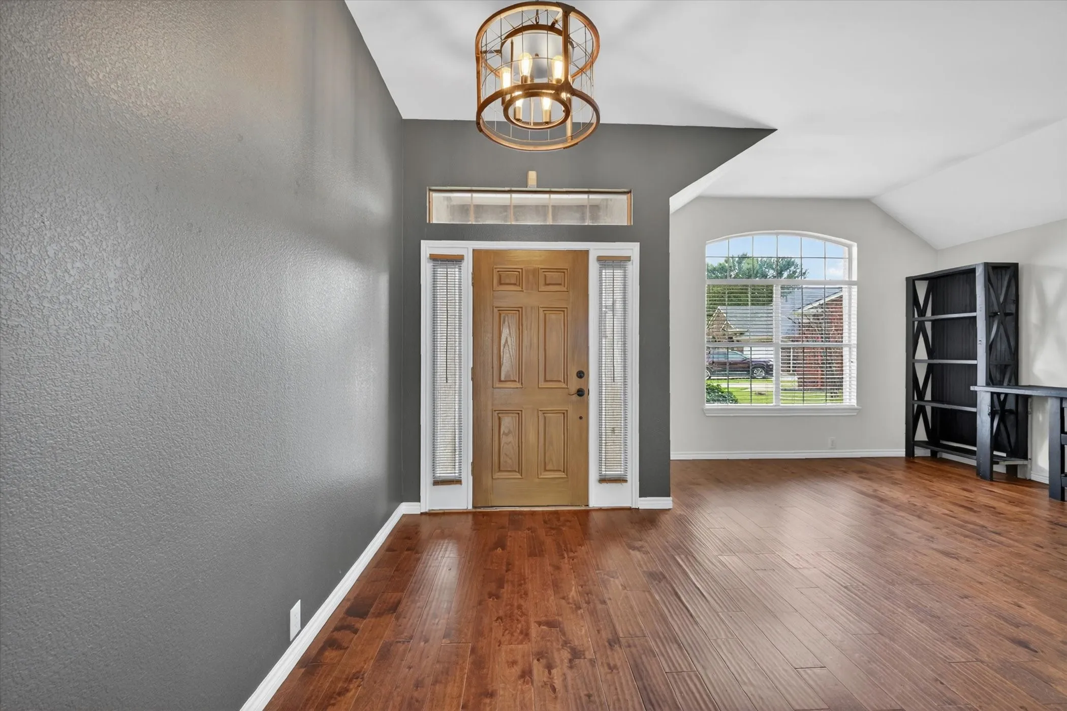 Wood-finish flooring, vaulted ceiling, arched window, and a decorative ceiling fixture