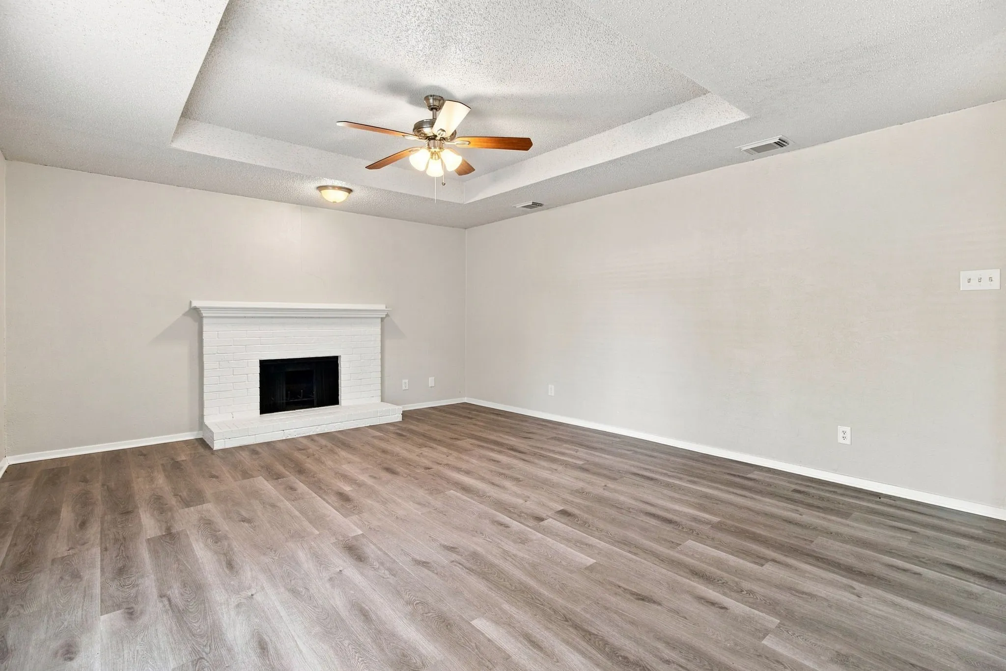 Recessed ceiling detail, wood-finish flooring, white brick fireplace, ceiling fan with light fixture, flush mount lighting