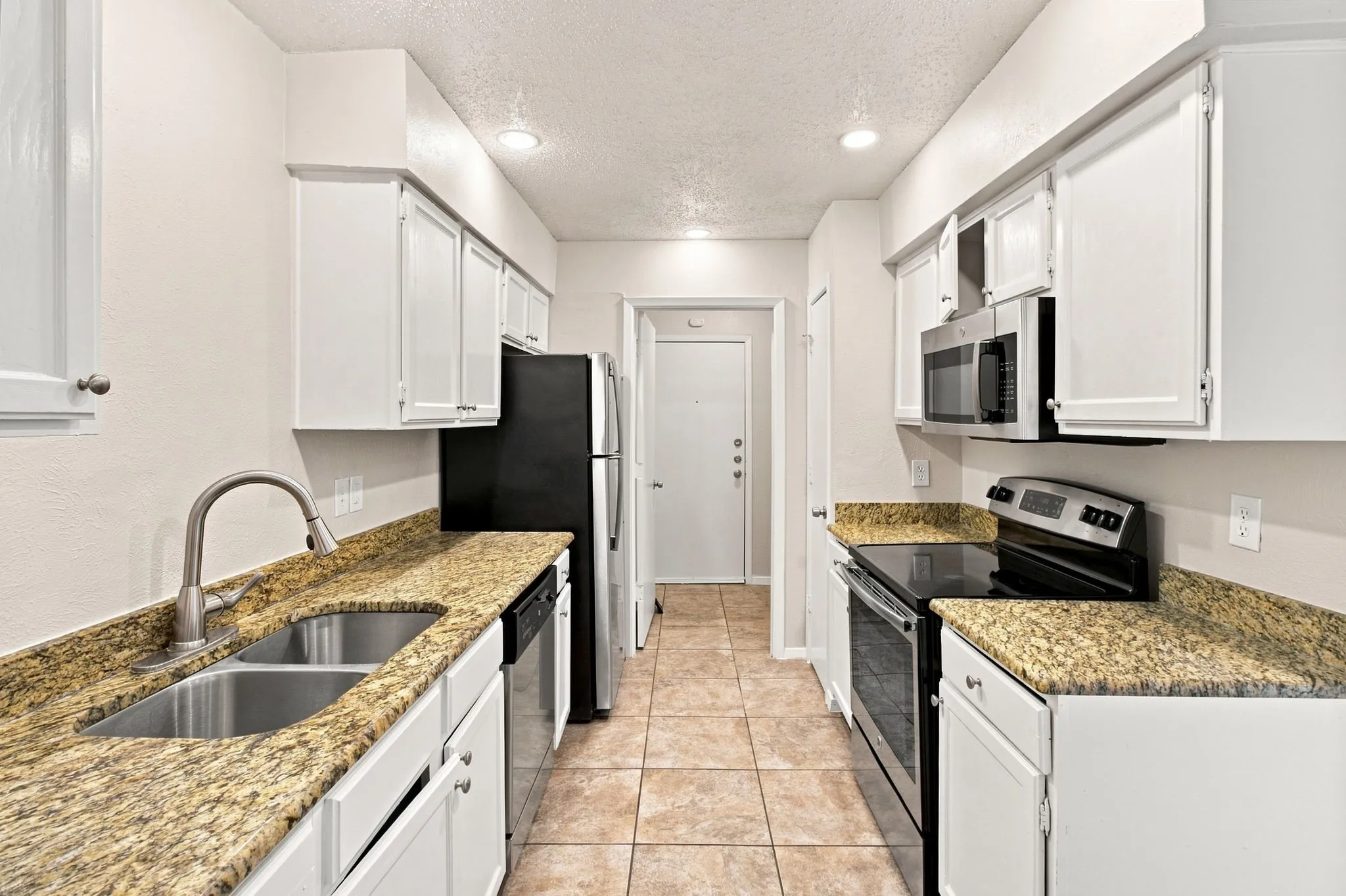 Galley-style kitchen featuring white cabinetry, granite countertops, stainless steel appliances including a gas range and microwave, undermount sink with gooseneck faucet, tile flooring, and recessed lighting throughout