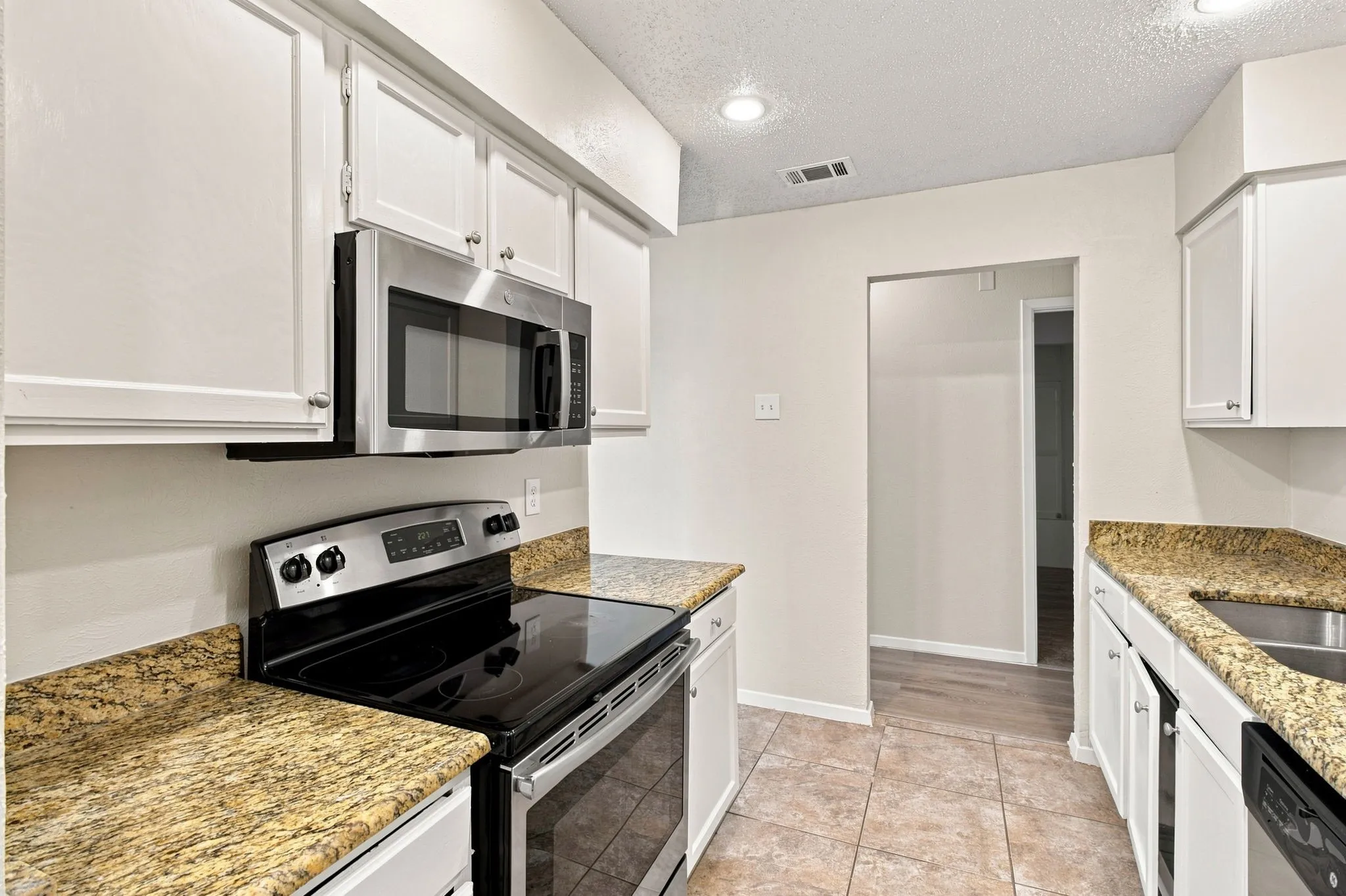 Kitchen featuring white cabinetry, granite-style countertops, stainless steel appliances, and tiled flooring