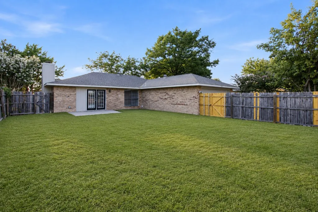 Expansive manicured lawn with mature landscaping, bordered by wooden privacy fencing