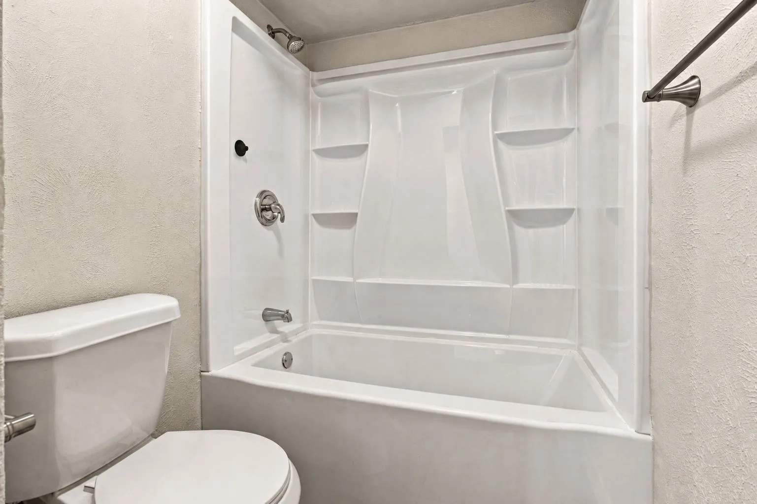 White bath and shower combination unit featuring integrated shelving