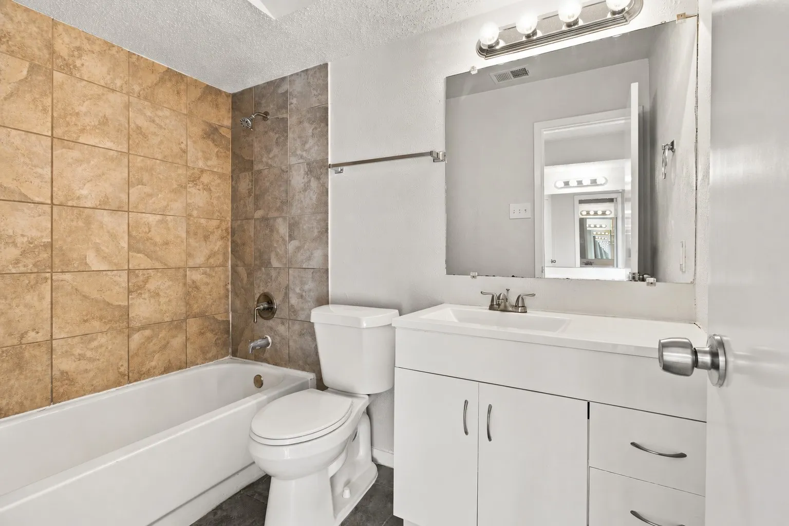 Bathroom featuring a built-in bathtub with tiled surround, a white toilet, and a vanity with an integrated sink and base cabinetry