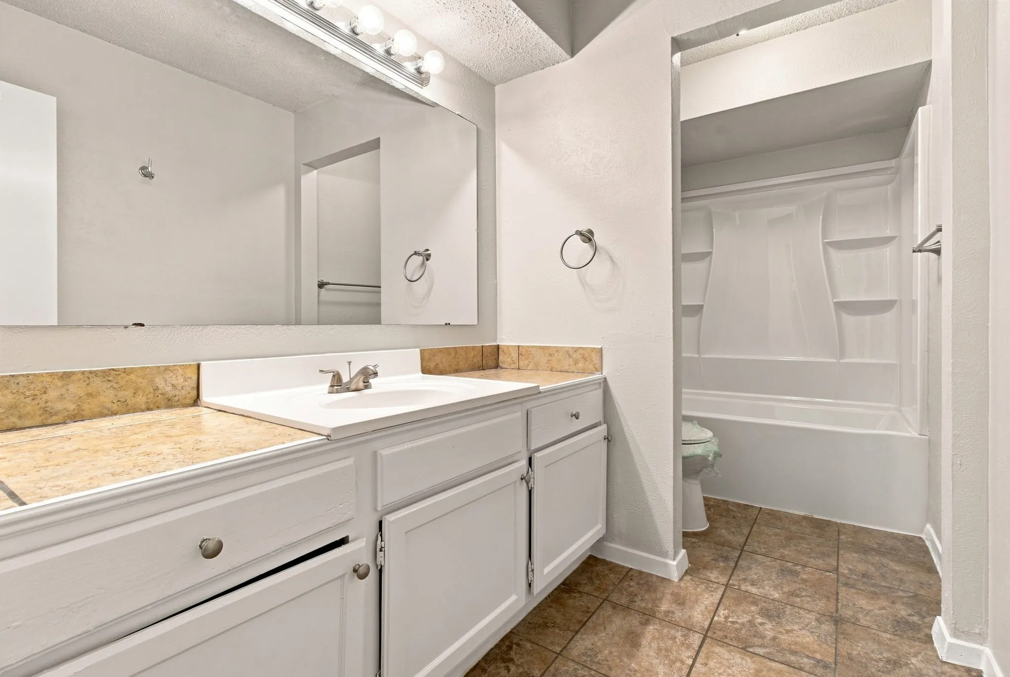 White vanity with an integrated sink and brushed nickel faucet, large vanity mirror, and light-colored countertop