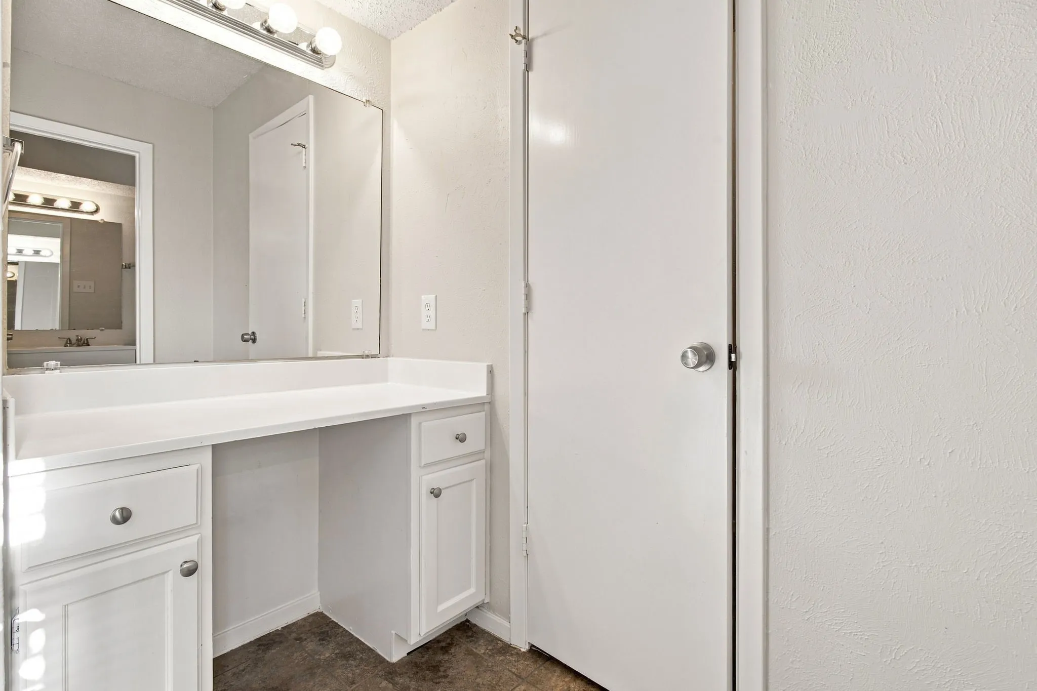 White vanity with built-in cabinetry, integrated countertop, overhead lighting, and wall-mounted mirror