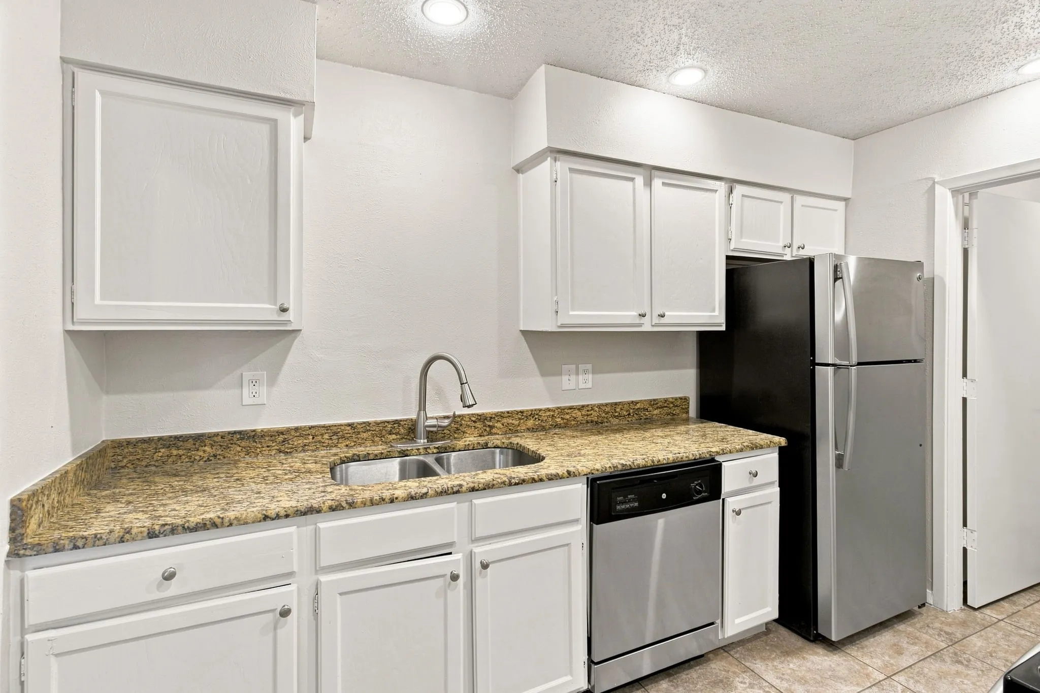 Kitchen featuring white cabinetry, a double basin stainless steel sink, a stainless steel dishwasher, a stainless steel refrigerator, and speckled countertops