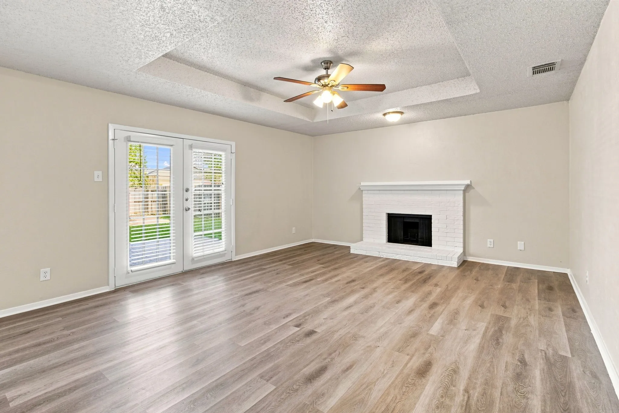 Spacious room featuring wood-finish flooring, a white brick fireplace, and dual French doors opening to the exterior