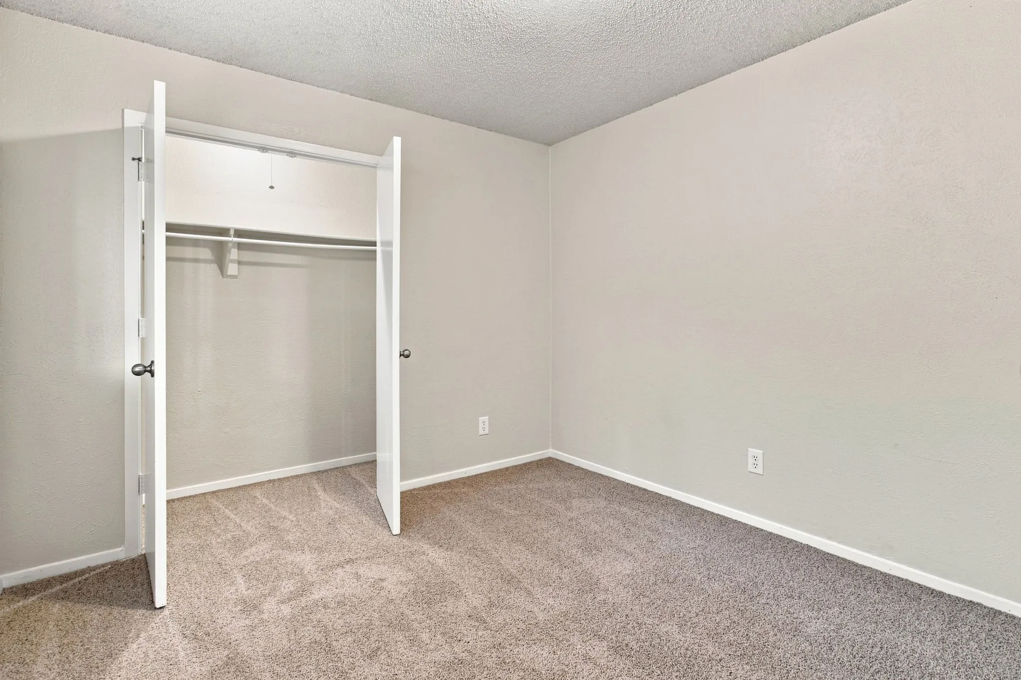 Neutral tone painted walls with textured ceiling, light-colored carpeting, and a built-in closet with double bifold doors