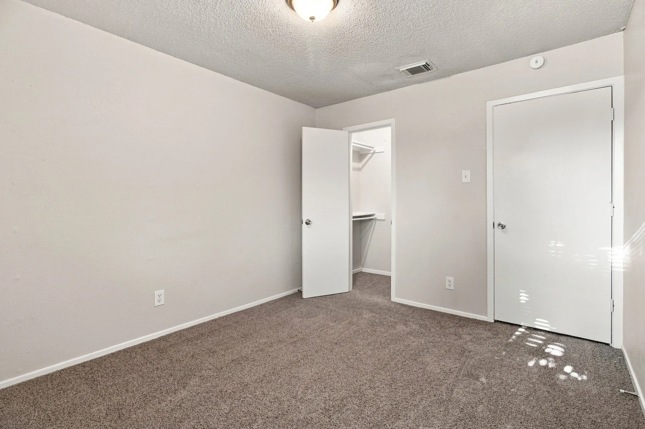 Wall-to-wall carpeting in a neutral tone, ceiling-mounted light fixture, and a built-in closet with shelving