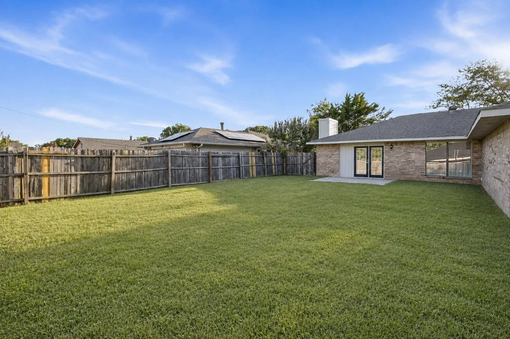 Expansive backyard featuring a manicured lawn, mature landscaping, and wooden privacy fencing