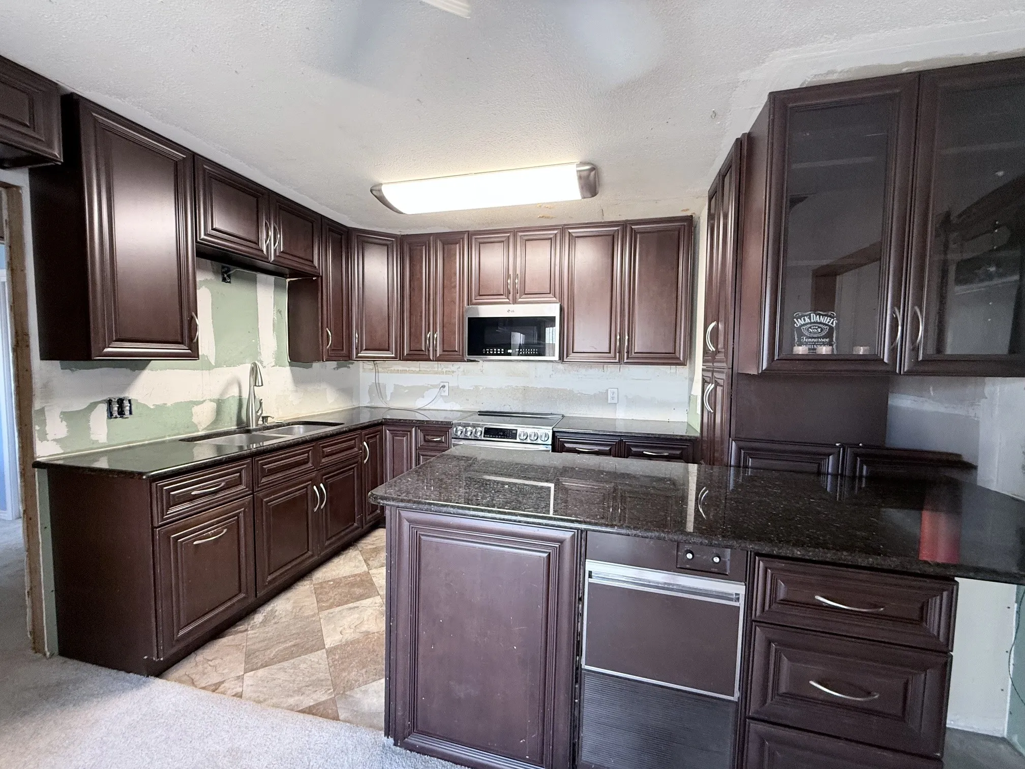Dark wood-finish cabinetry with silver hardware, dark countertops, built-in stainless steel microwave, and a stainless steel oven