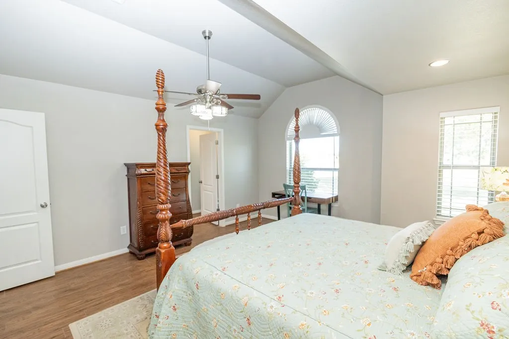 Vaulted ceiling, wood-finish flooring, ceiling fan with integrated lighting, arched window, and recessed lighting