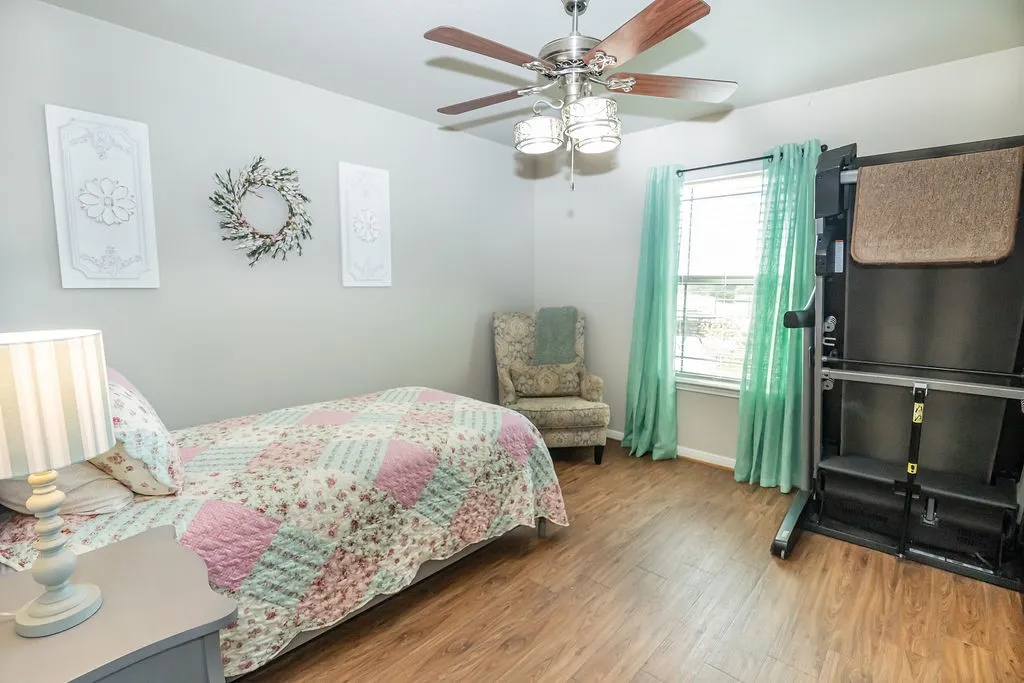 Wood-finish flooring, ceiling fan with light fixture, single window with blinds, and light gray wall paint