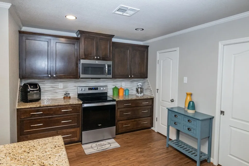Wood-finish flooring, dark wood cabinetry, stainless steel appliances, stone countertops, and a tile backsplash