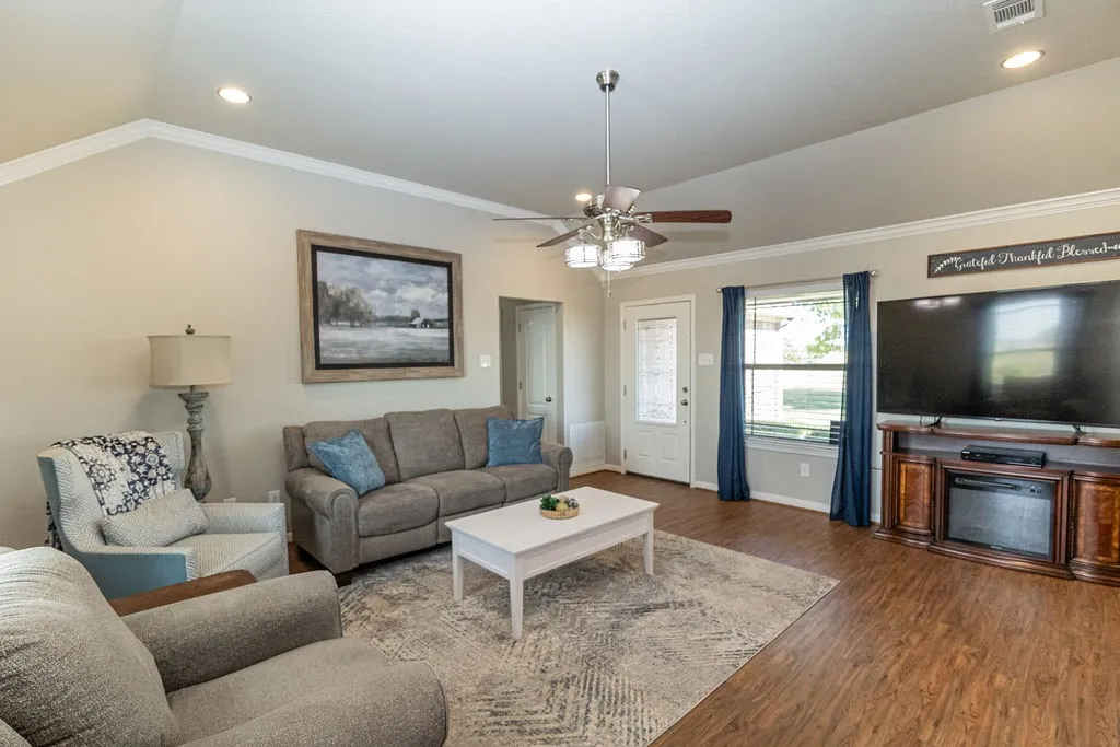 Spacious living room showcasing hardwood flooring, a ceiling fan with integrated lighting, and built-in entertainment cabinetry with a mounted flat-screen television