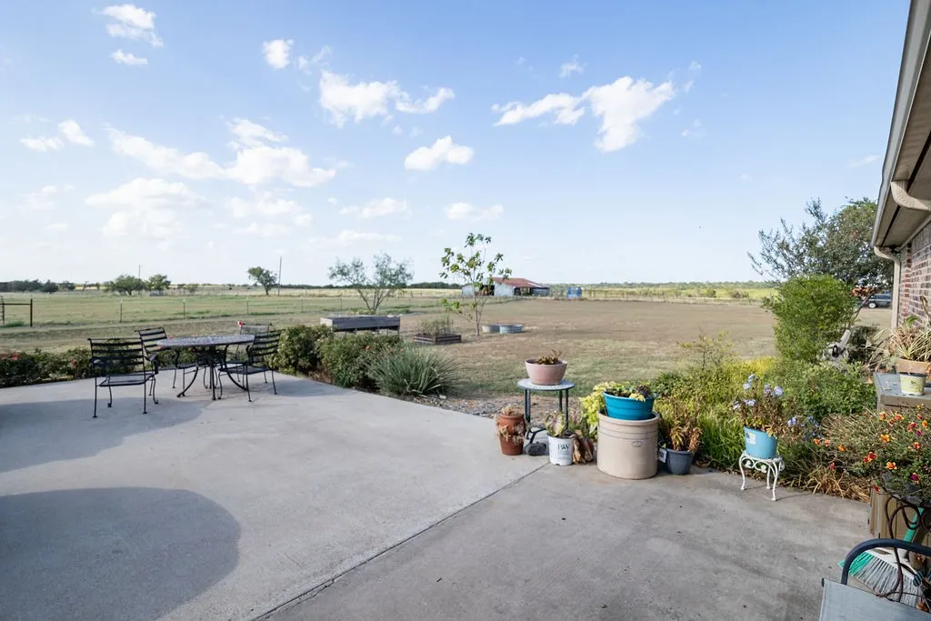 Expansive concrete patio with surrounding landscaping and a wide open field