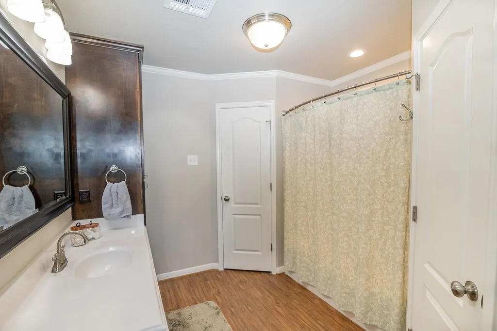 Wood-finish flooring, white vanity with dual sinks, brushed nickel fixtures, built-in dark wood cabinetry, and white paneled doors