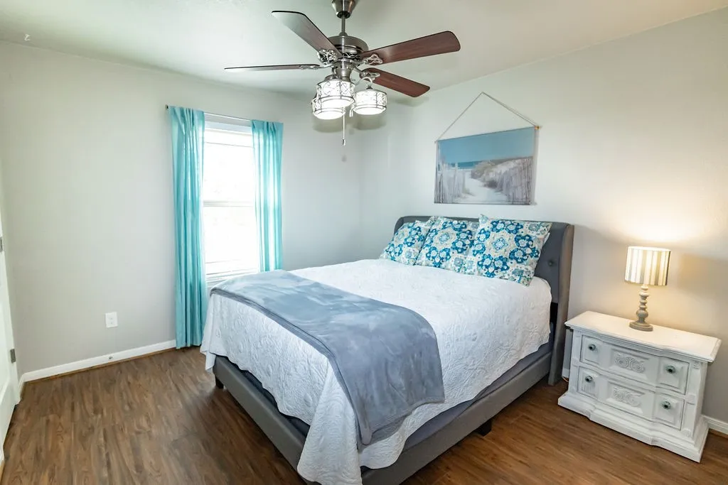 Wood-finish flooring, ceiling fan with integrated lighting, window with blinds, and white trim