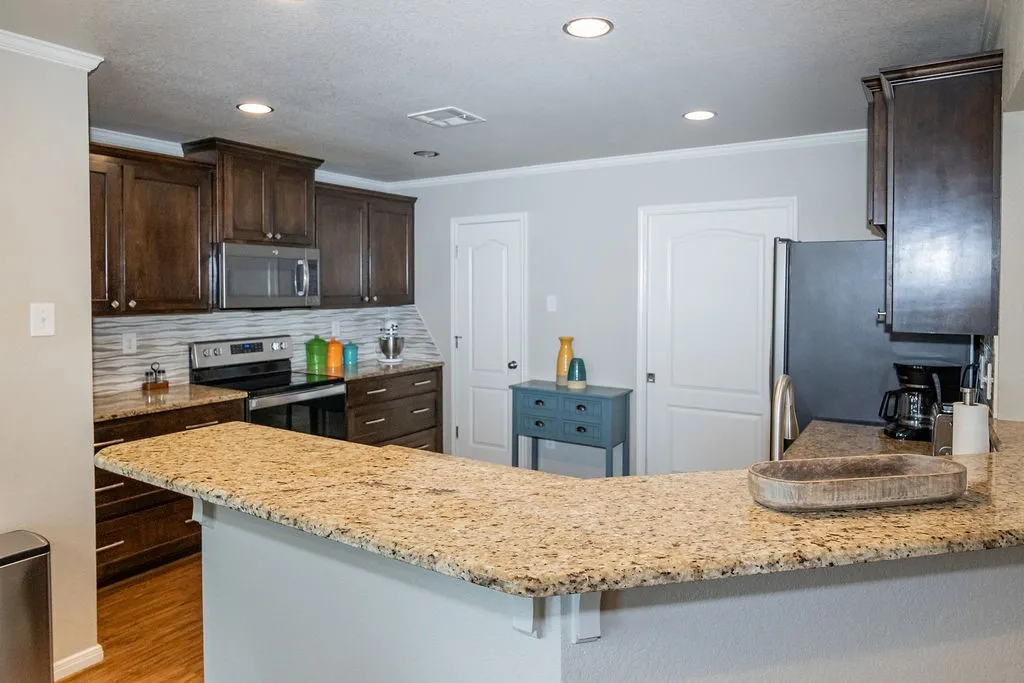 Kitchen featuring granite countertops, dark wood-finish cabinetry, stainless steel appliances, and a tiled backsplash