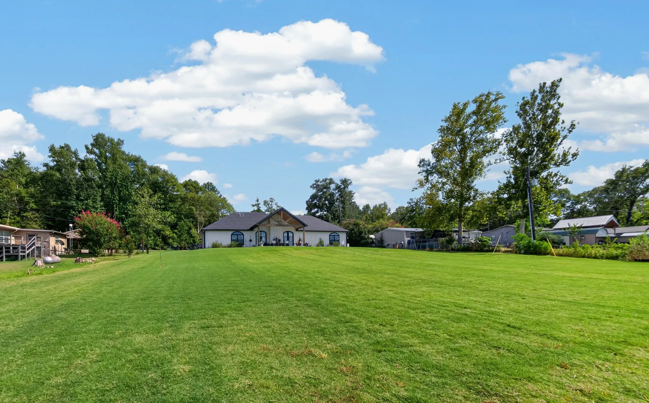Expansive green lawn with mature trees and a single-story residence featuring a dark roof and arched window