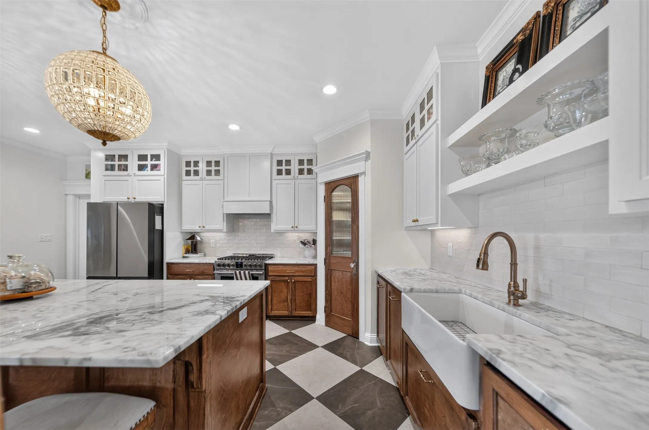 White upper cabinetry with glass inserts, wood-finish lower cabinetry, marble countertops, farmhouse sink, and a black and white checkerboard floor